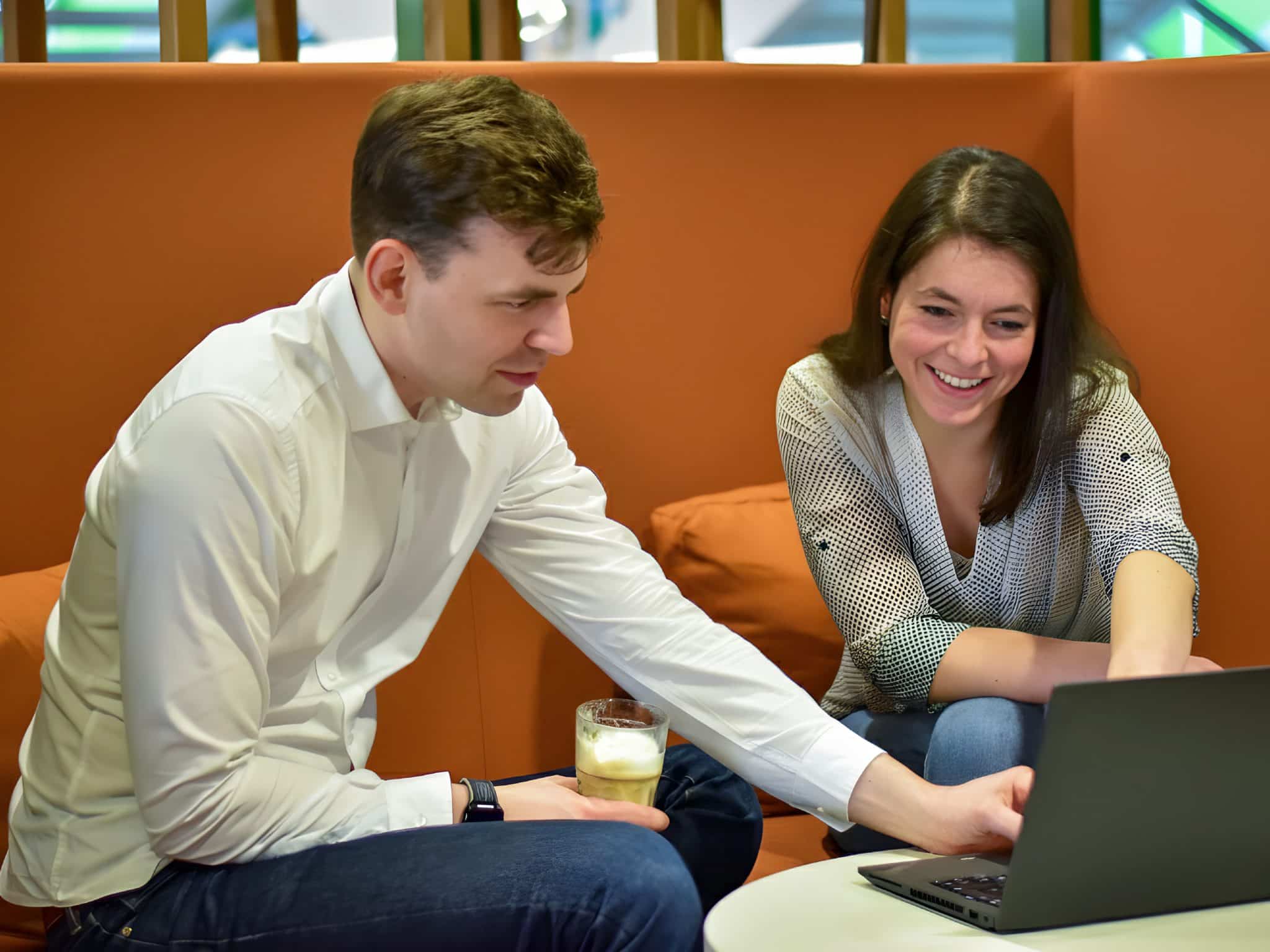 Zwei Personen von IPS arbeiten zusammen auf einer orangefarbenen Couch.